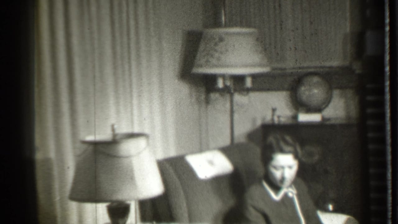 Woman in an armchair looking down with living room lamps and globe behind her.
