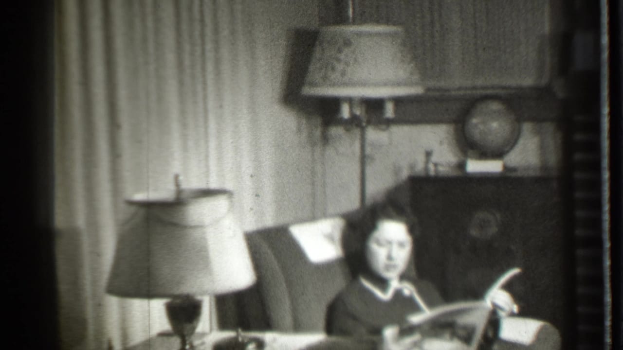 Woman seated in a living room reading a magazine beside a table lamp.