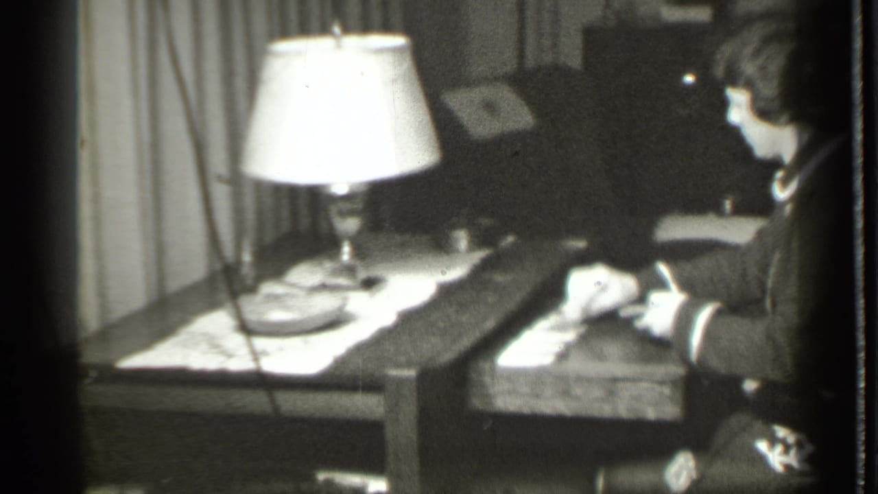 In 1939 Danielson, Connecticut home-movie footage, a woman sits at a table with playing cards under a bright lamp.