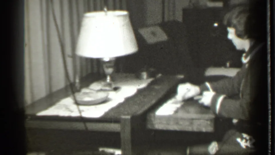 In 1939 Danielson, Connecticut home-movie footage, a woman sits at a table with playing cards under a bright lamp.