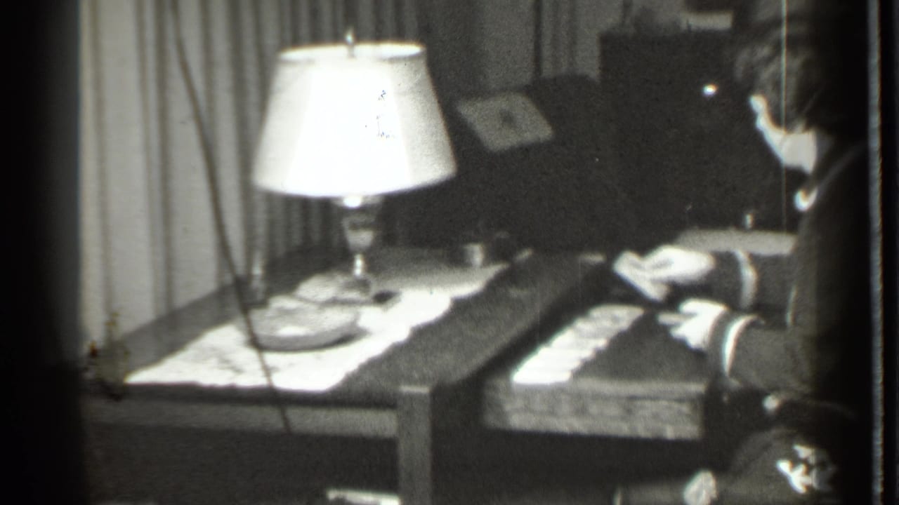 Woman at the right edge reaches toward cards spread on a lamp-lit table.