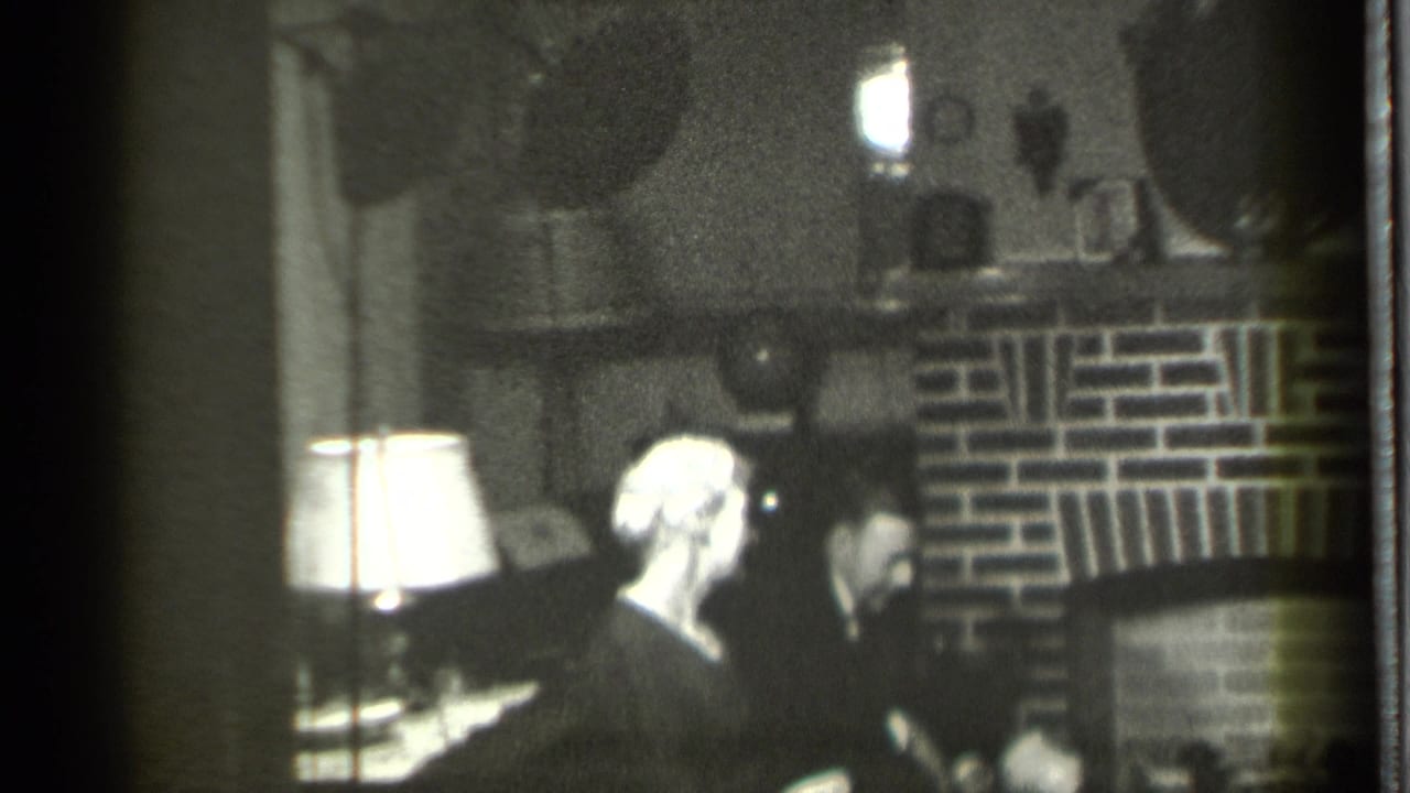 A 1939 Danielson home interior shows adults seated near a brick fireplace, with a white-shaded lamp providing the main light.