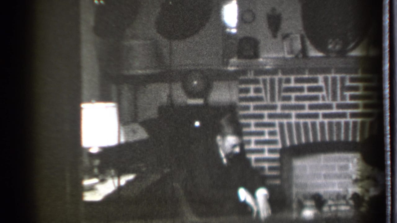 In a 1939 Danielson, Connecticut home-movie frame, a seated man looks down near a brick fireplace and glowing table lamp.