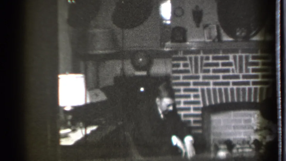 In a 1939 Danielson, Connecticut home-movie frame, a seated man looks down near a brick fireplace and glowing table lamp.
