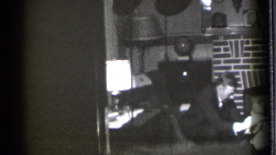 The closing frame shows the suited man seated in the Danielson den, with the lamp and brick fireplace behind him and a toddler partly visible.