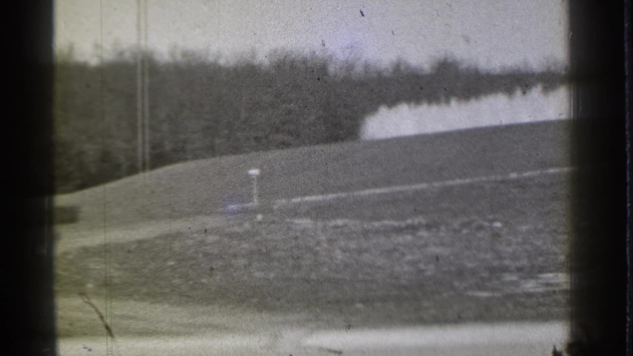 Sloping golf course with a small white marker, distant trees, and a pale fountain or water feature.