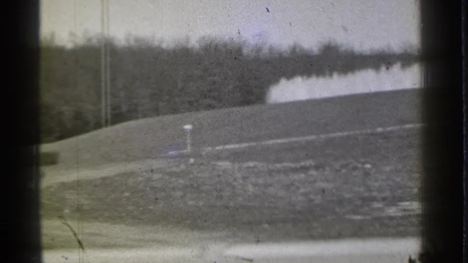 1939 Danielson, Connecticut 8mm frame showing a sloped golf course, marker post, distant tree line, and pale fountain or water feature.