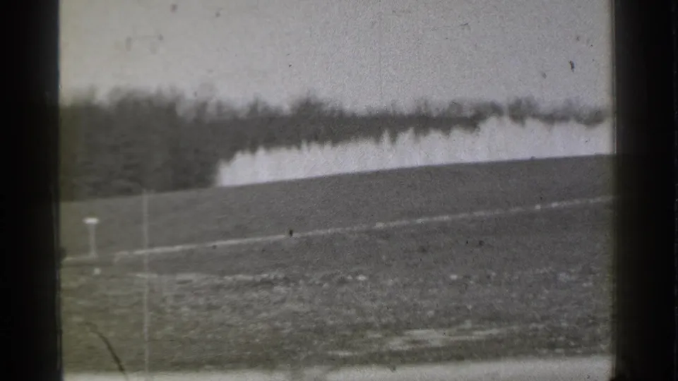 1939 Danielson, Connecticut golf course frame with sloped grass, a small marker post, tree line, and pale water feature in soft focus.