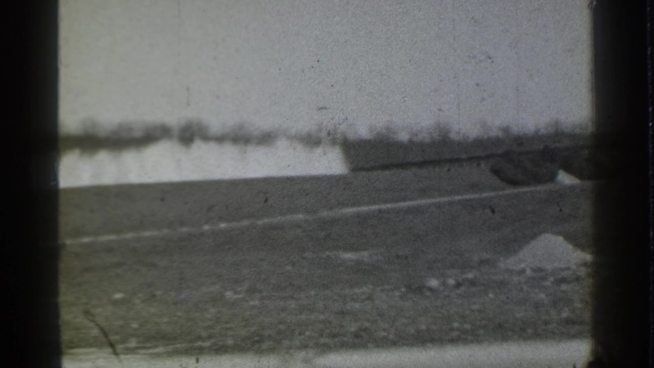 The pan reveals open ground in Danielson with a pale boundary and the edge of a low industrial structure at right.