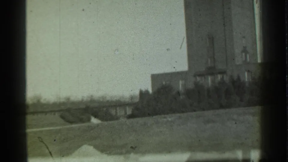 1939 Danielson, Connecticut home-movie frame showing a tall brick tower partly cropped beside low buildings, trees, grass, and bright sky.