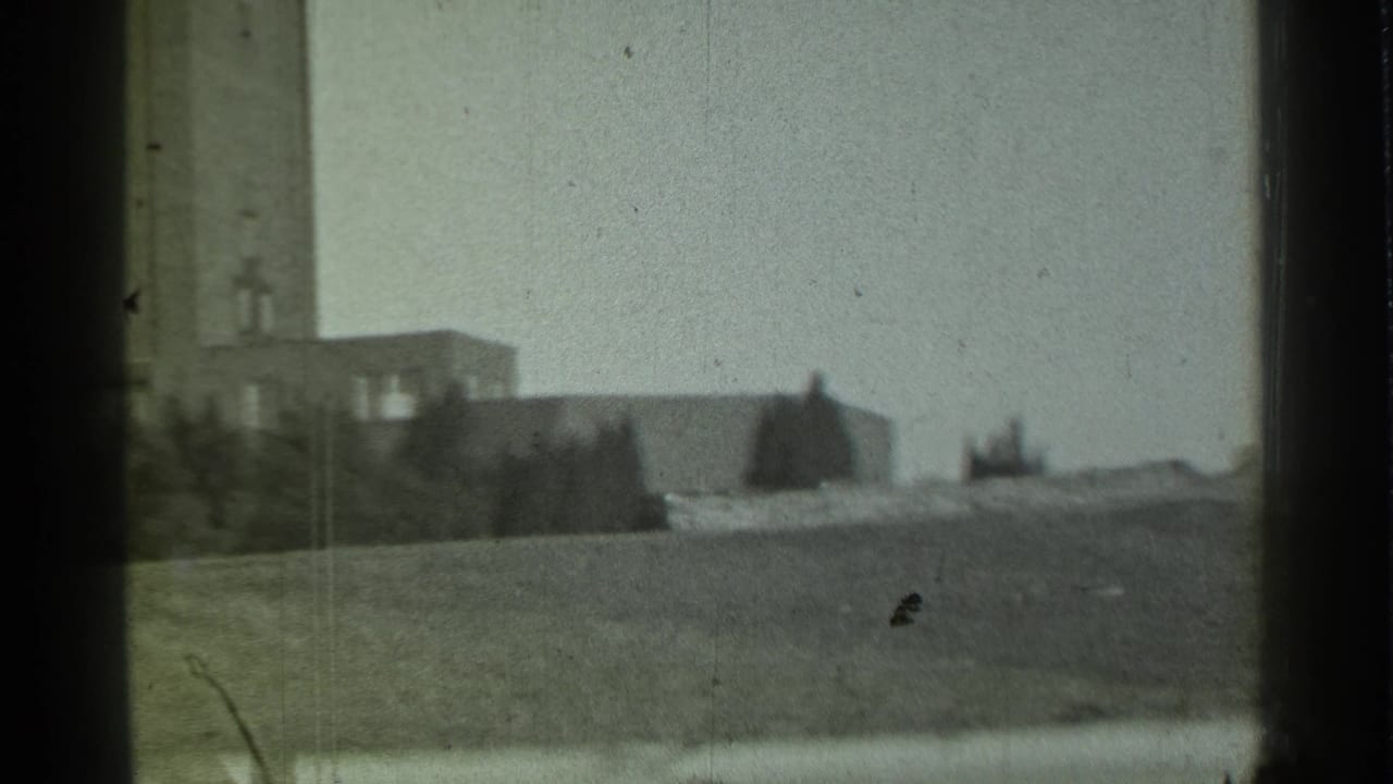 Distant towered building on a grassy hill seen through a window frame.