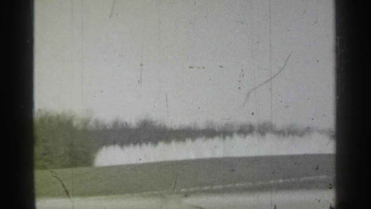 Soft exterior view with pale sky, distant tree line or building, and dark frame borders.