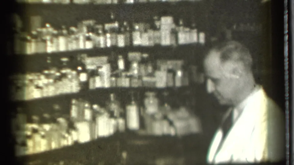 In a 1939 Danielson, Connecticut pharmacy interior, a white-coated man stands near shelves stocked with bottles and medicine containers.