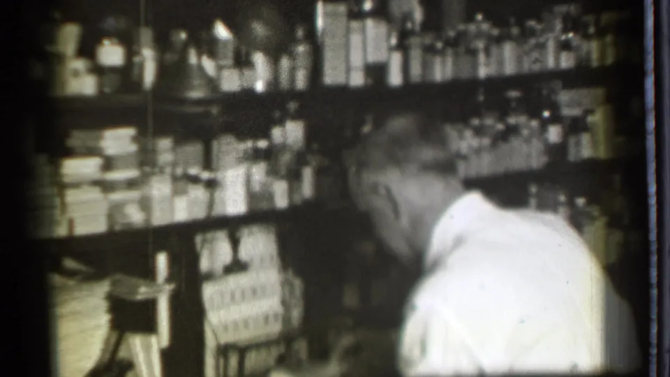 The closing frame shows the white-coated worker leaning forward near stocked pharmacy shelves in the Danielson, Connecticut interior.