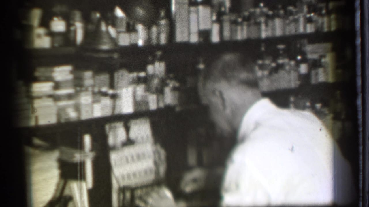 Man in a white shirt stands behind shelves filled with bottles and boxes.