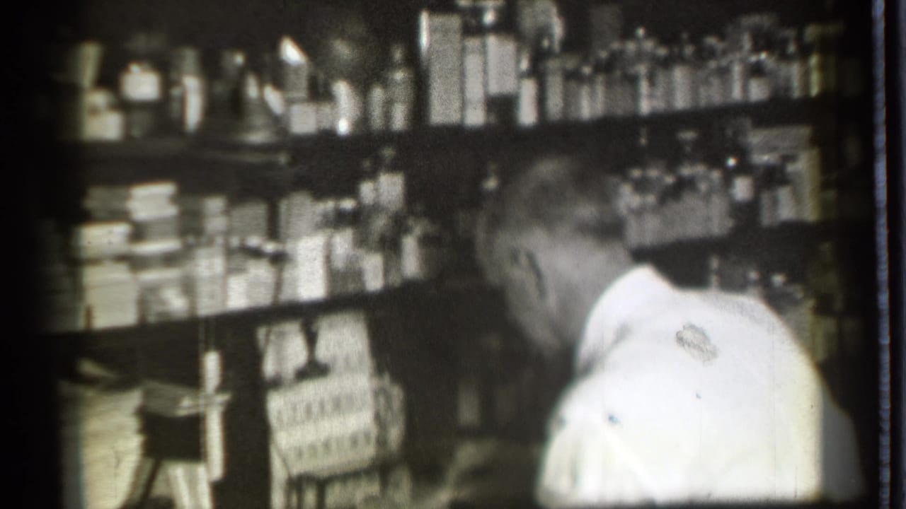 Man leans near a counter with shelves of bottles and boxes behind him.