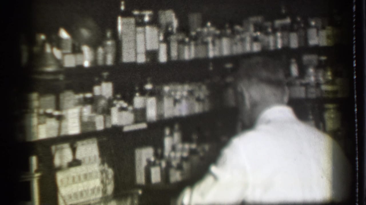 Man seen from behind beside shelves of medicine bottles and boxes.