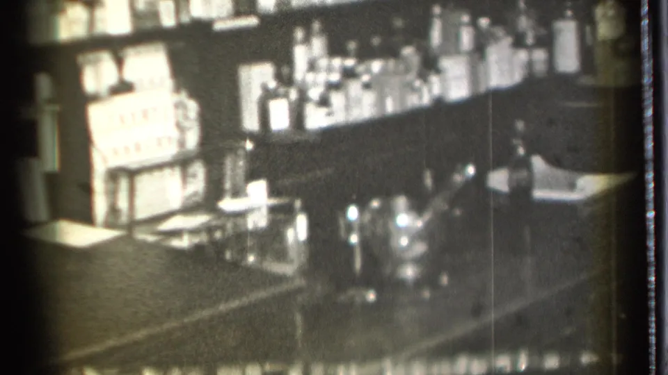 The final frame shows the pharmacy-like interior without a clear face, emphasizing shelves, boxed goods, bottles, and glassware on the counter.