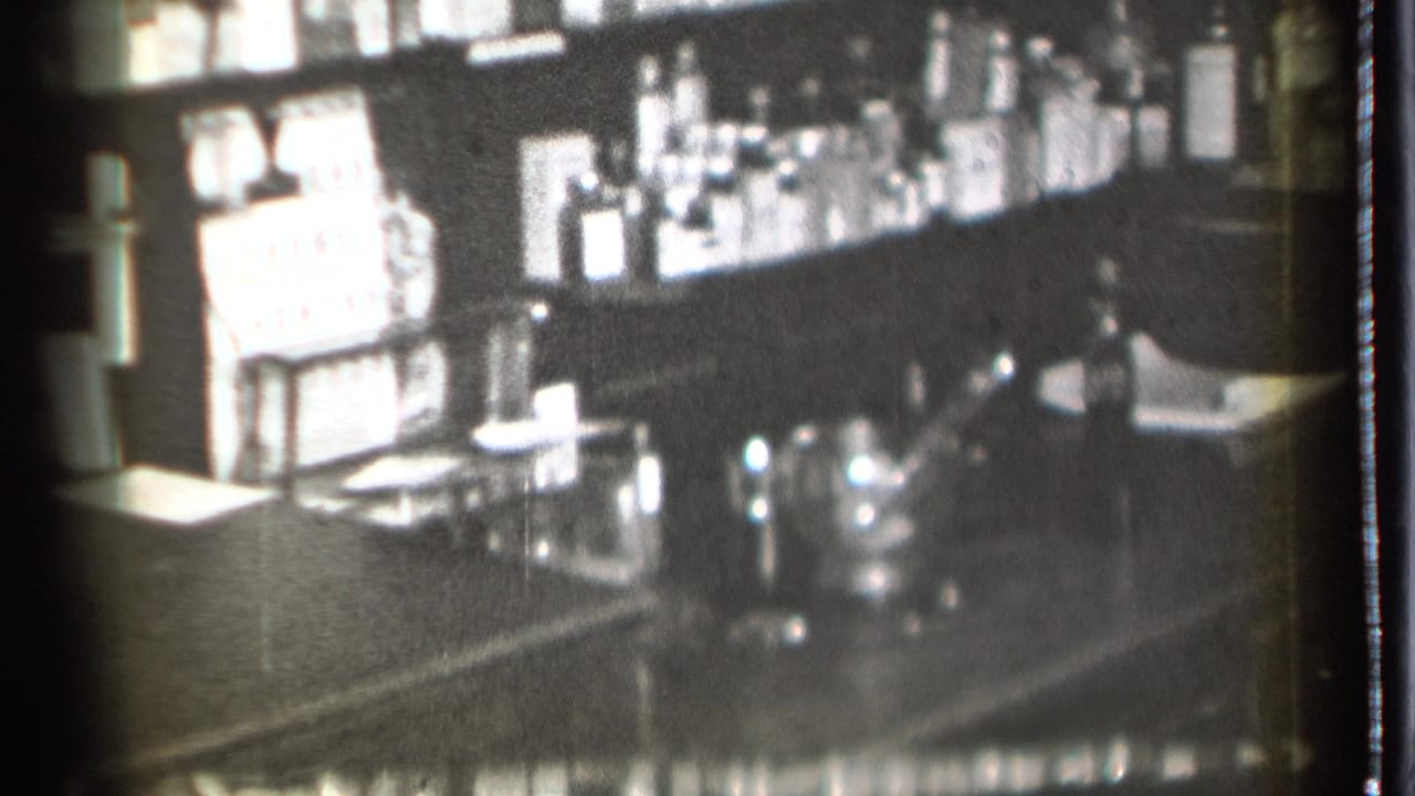 1939 8mm home-movie frame from Danielson, Connecticut, showing a dim bar counter with bottles, glasses, and a shaker in soft focus.