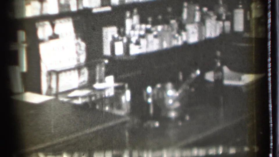 1939 8mm home-movie frame from Danielson, Connecticut, showing a dim bar counter with bottles, glasses, and a shaker in soft focus.