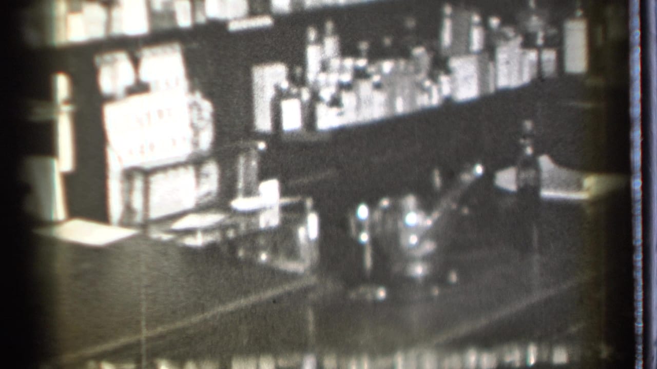 Bar shelves and counter with bottles, reflective glassware, and a dark background.