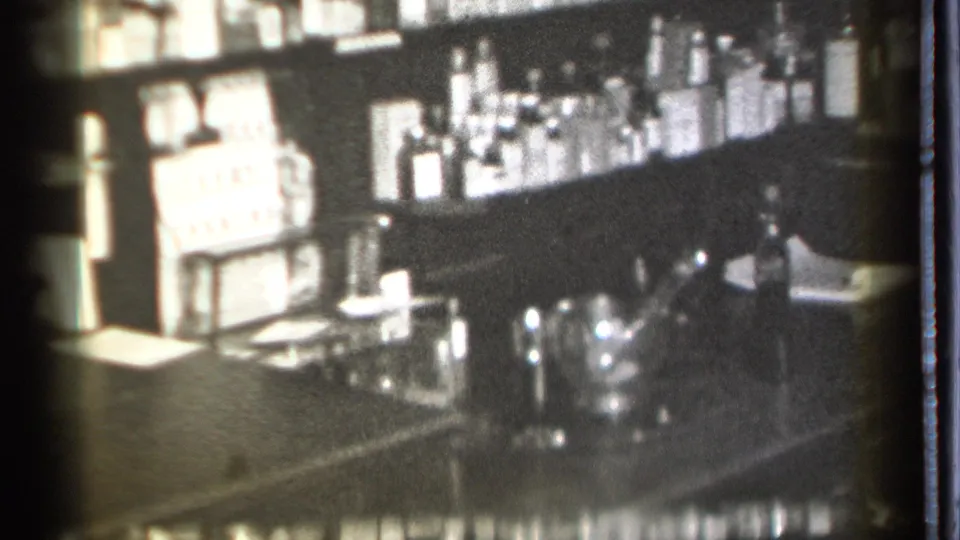 Grainy 1939 home-movie frame showing a Danielson pub counter area with clustered glassware, bottles, and reflective bar equipment.