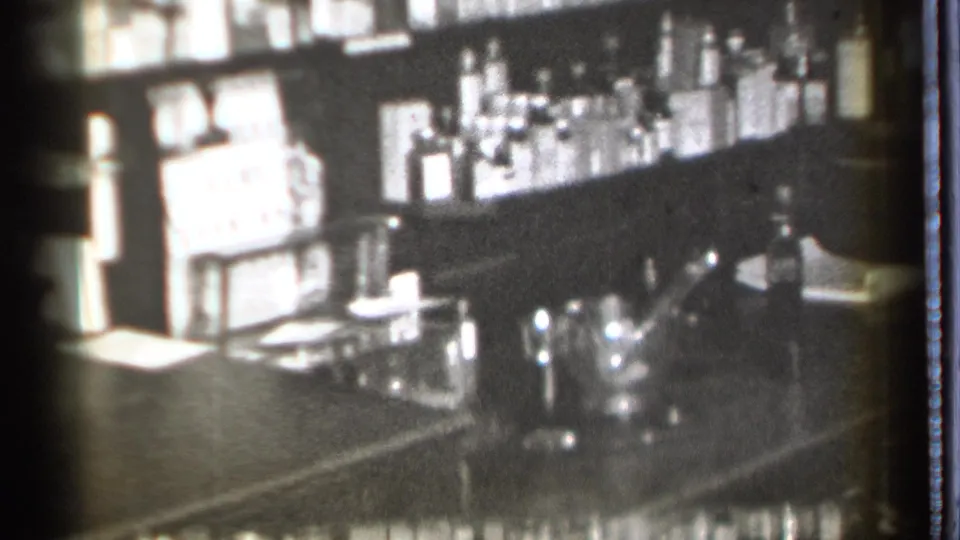Final 8mm frame of the Danielson bar interior, with liquor bottles, glassware, and counter surfaces softened by grain and exposure.