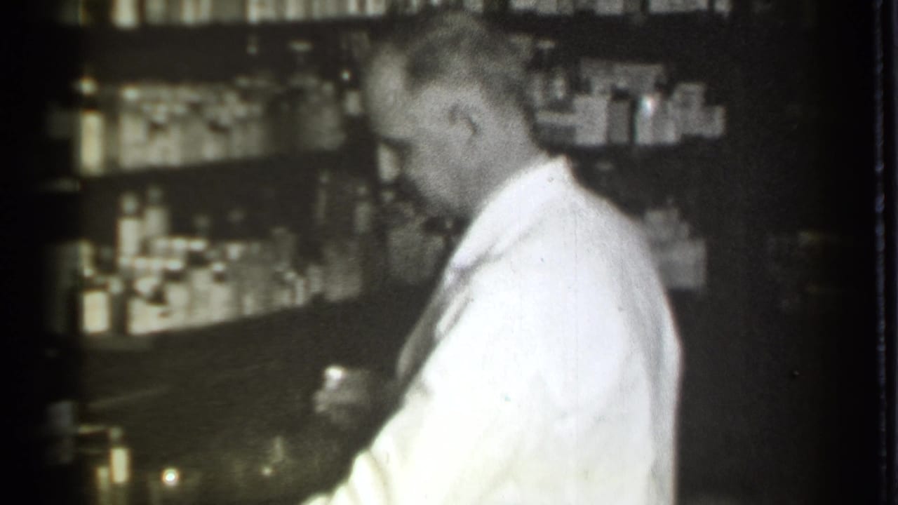 Pharmacist looks down while holding a small container near a pharmacy counter.