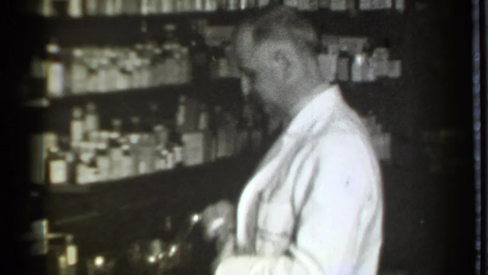 A side view shows the pharmacist at the counter in the Danielson pharmacy, surrounded by shelves of jars and bottles.