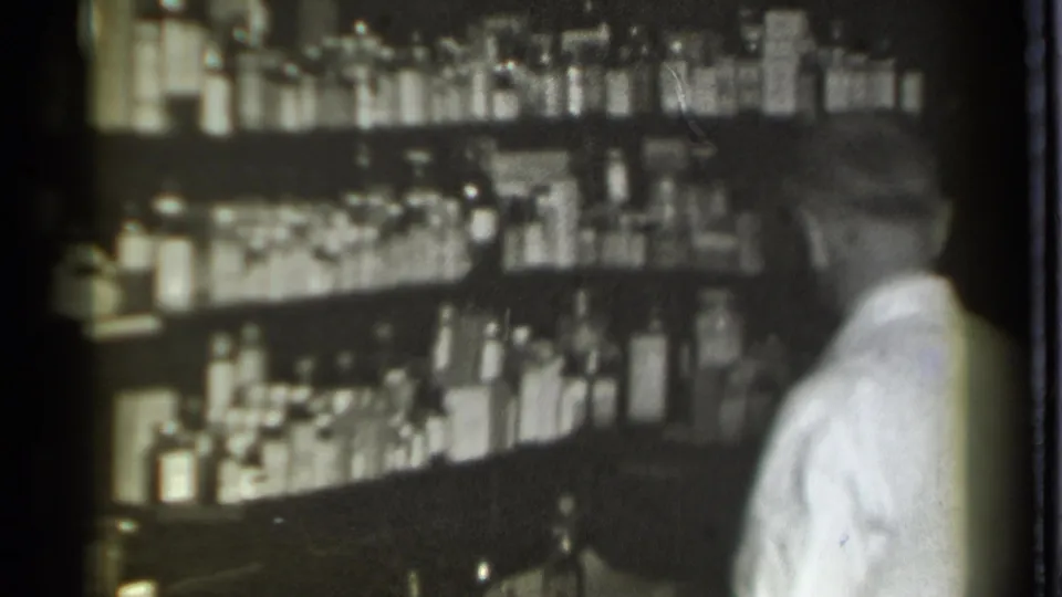 The final frame shows the pharmacist turned toward rows of bottles in the 1939 Danielson drugstore interior.