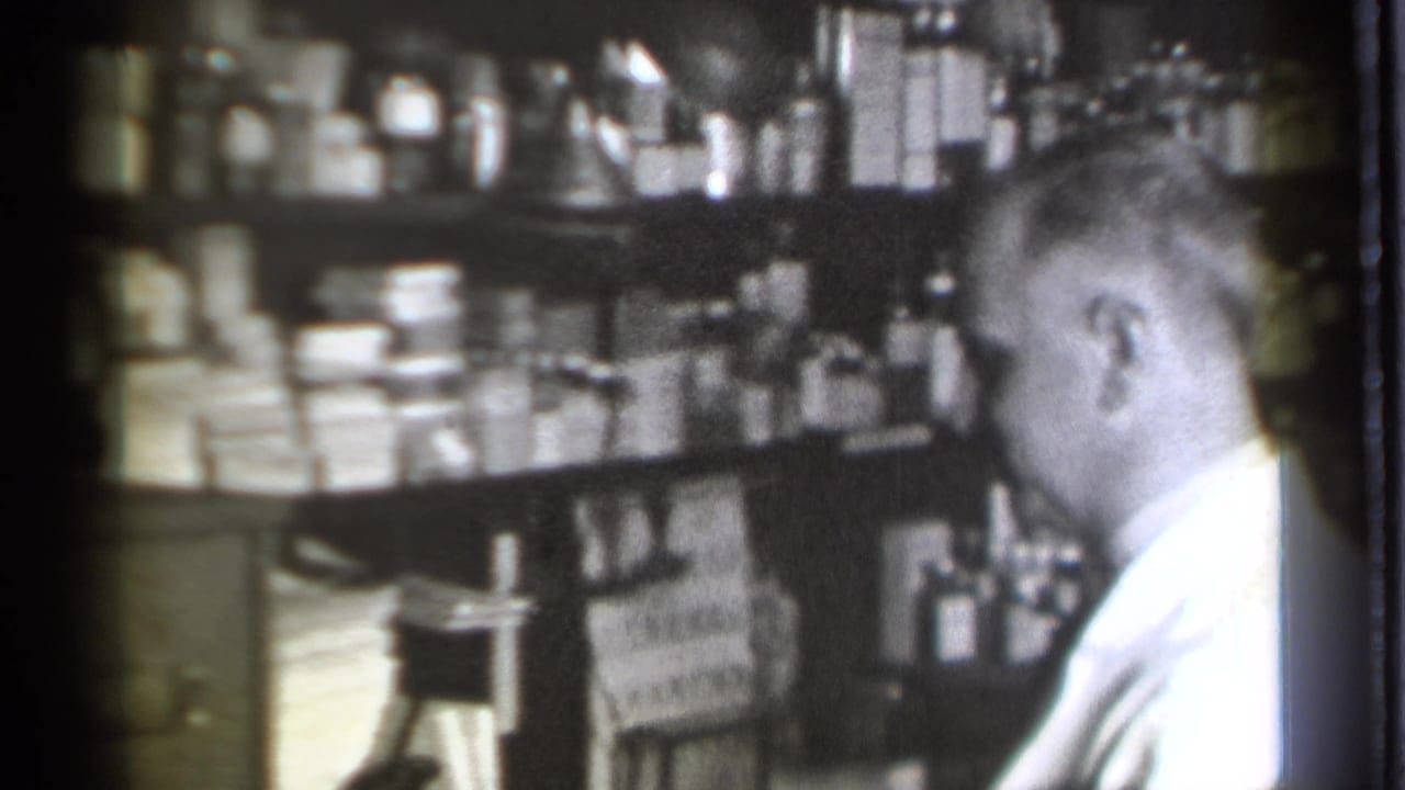 Pharmacist faces shelves of boxed medicines and bottles inside a drugstore.