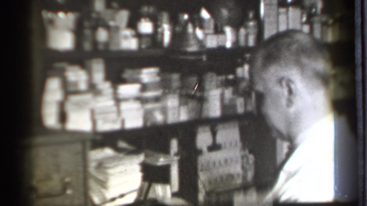 In a Danielson, Connecticut drugstore interior from 1939, a pharmacist in a white coat stands near shelves of bottles and boxed medicines.