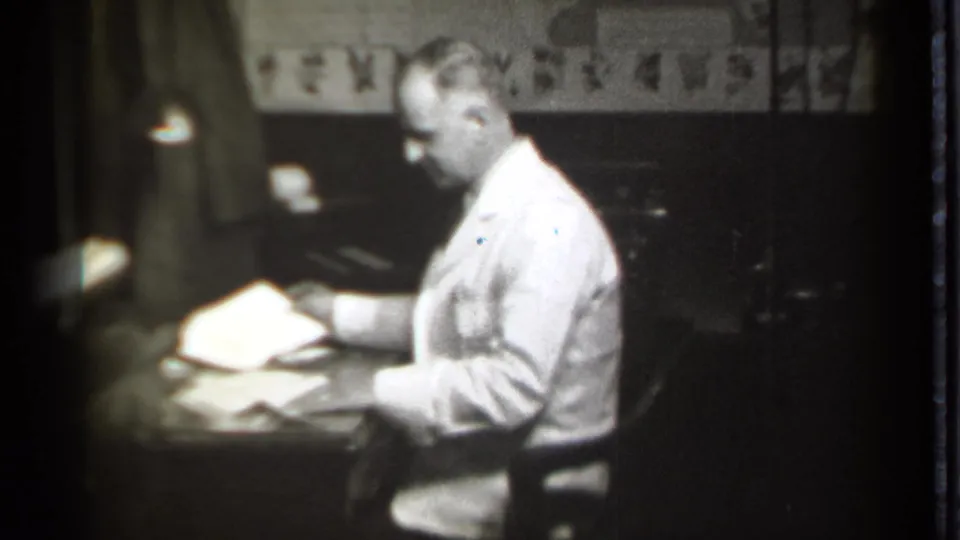 In Danielson, Connecticut, 1939 footage, a seated man in a light suit handles papers at a desk in a dark office.