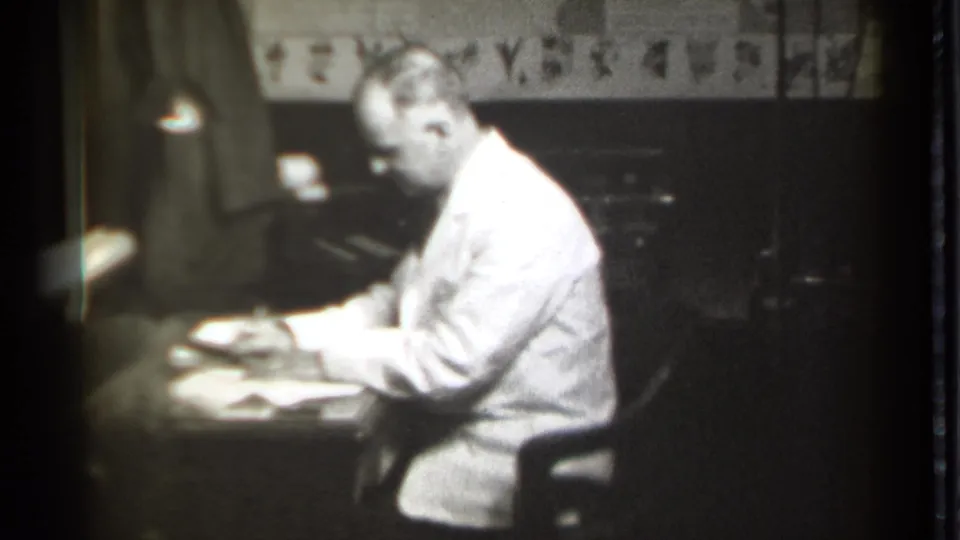 The man leans forward over documents, appearing to write or sign papers at an office desk in 1939 Connecticut footage.