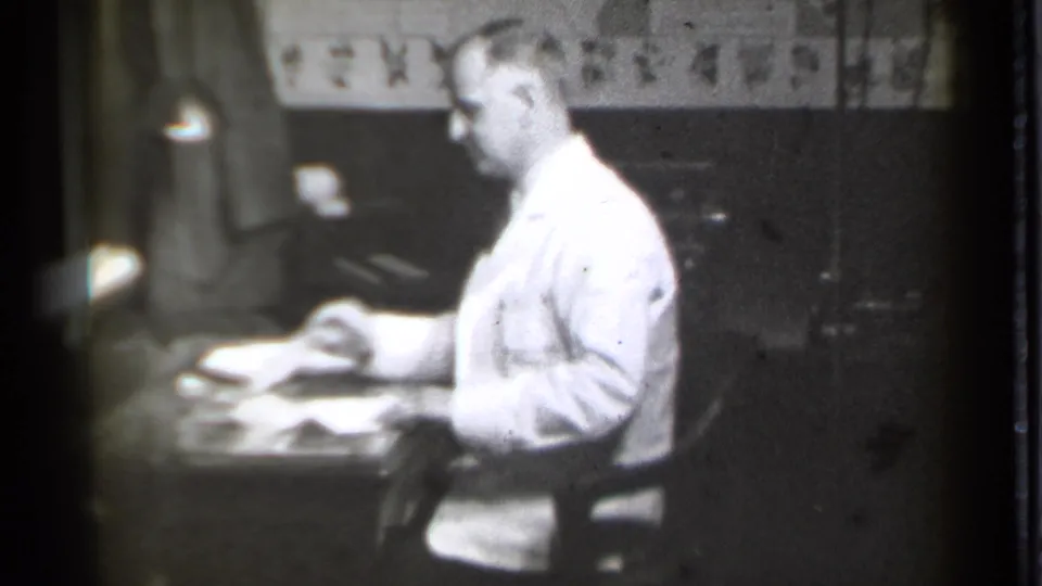 The man sits in profile at the office desk, appearing to adjust documents during the short 1939 Danielson home-movie clip.