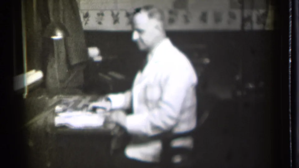 At the end of the clip, the man remains seated at the desk in the 1939 Danielson room, looking down at papers in soft 8mm focus.