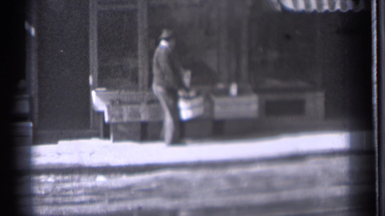 In Danielson, Connecticut, 1939, a man in a dark coat and hat appears to arrange items on a sidewalk counter outside a storefront.
