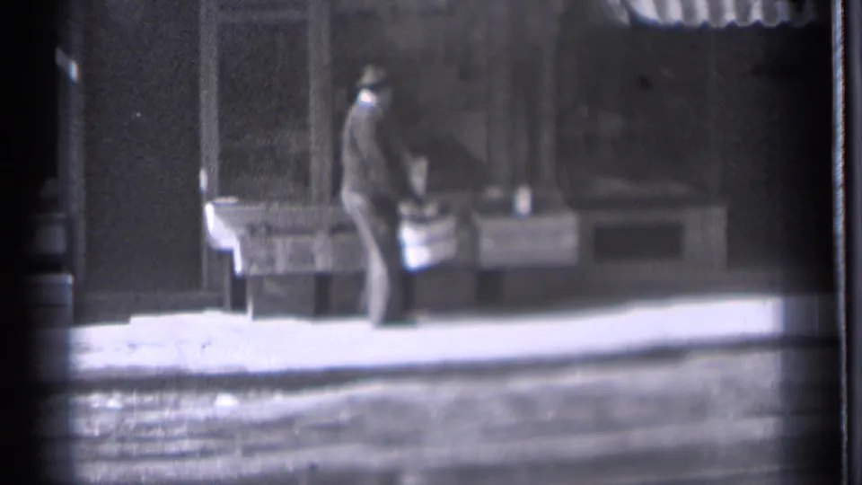 In Danielson, Connecticut, 1939, a man in a dark coat and hat appears to arrange items on a sidewalk counter outside a storefront.