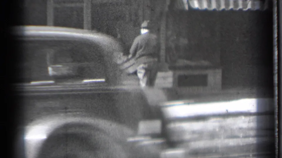 A passing car partly obscures the 1939 Danielson storefront scene as the man continues working beside the sidewalk display.