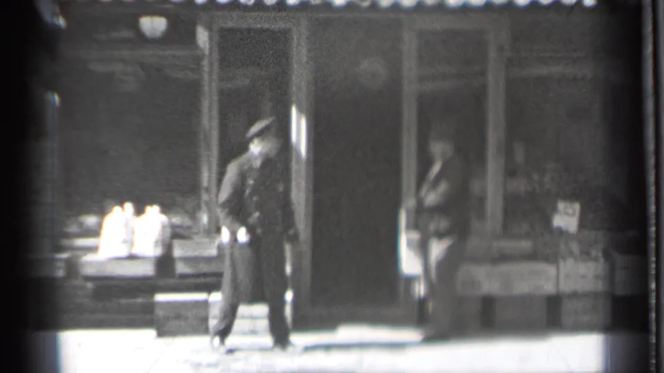 The uniformed man remains outside the Danielson storefront as the suited man moves near or into the doorway during the 1939 sidewalk encounter.