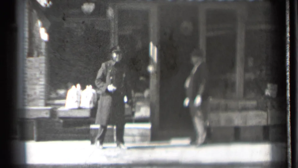 Outside the 1939 Danielson storefront, the uniformed man stands near displayed goods while another adult figure passes close to the doorway.