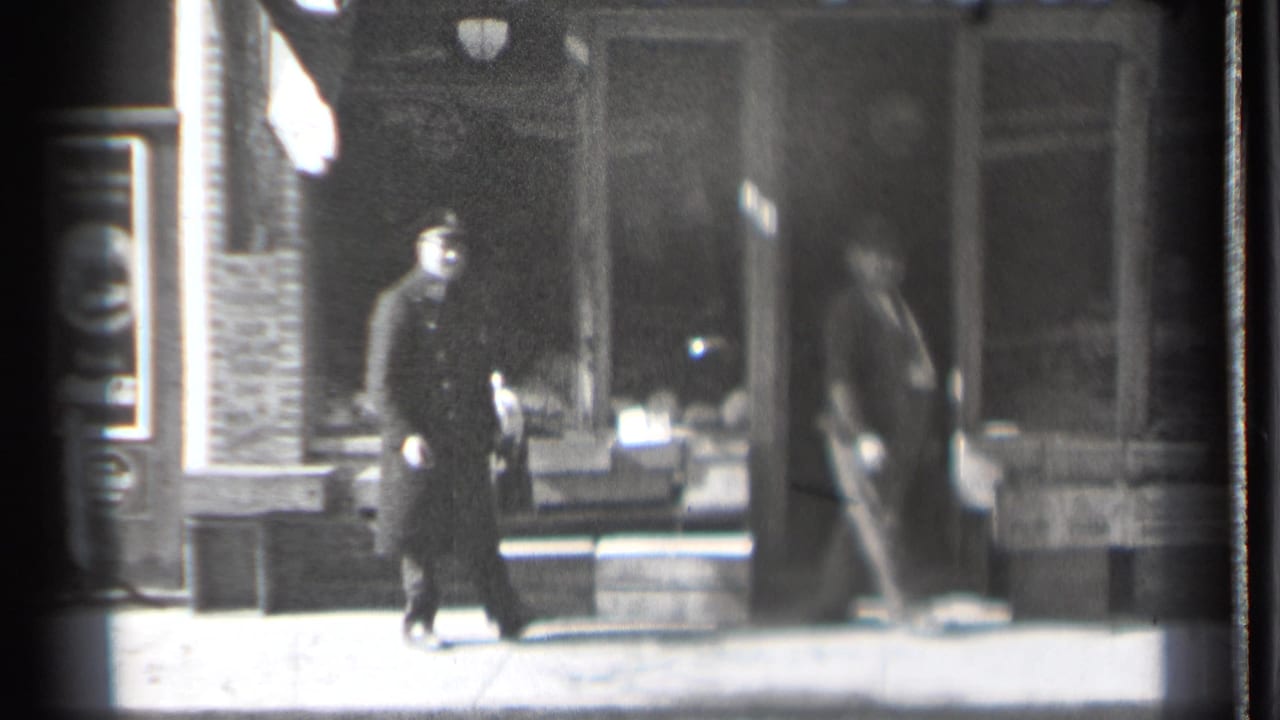 Two adult men on a sunny sidewalk in front of a brick storefront.