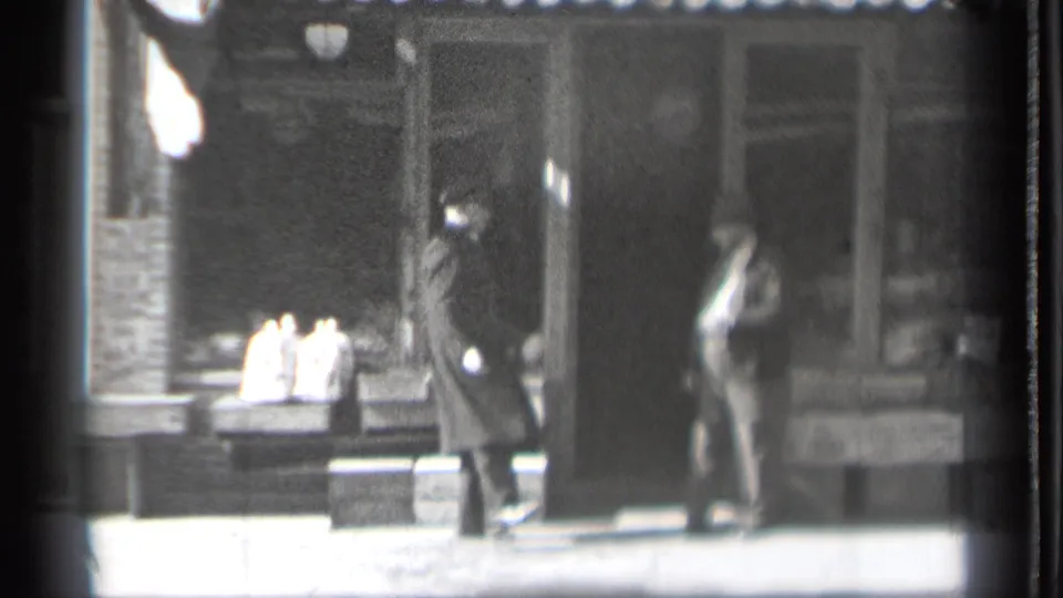 The 1939 Danielson street scene shows two adult men paused near a shopfront, with display-window objects and sidewalk detail visible in soft focus.