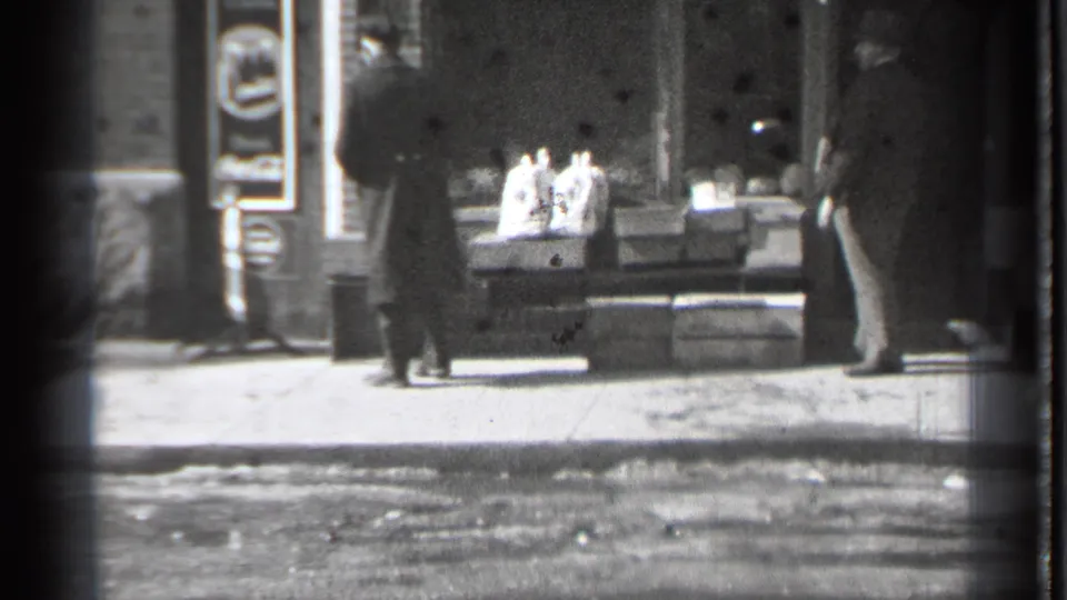 The final frame holds the storefront view as the two men stand apart on the Danielson sidewalk, with street surface and window display visible.
