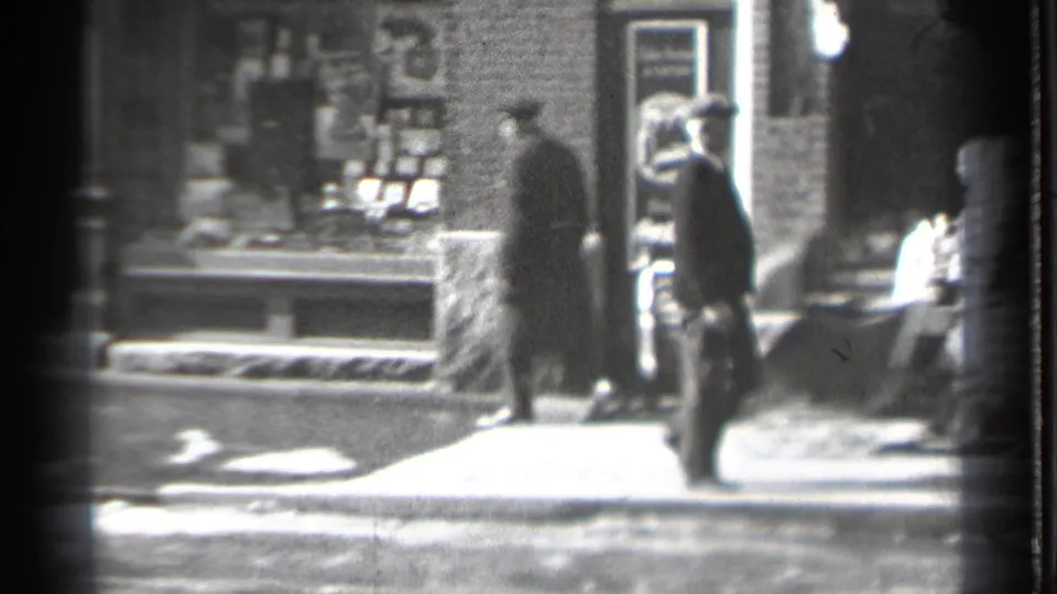 1939 Danielson, Connecticut sidewalk view with bundled pedestrians moving past brick storefronts and display windows.