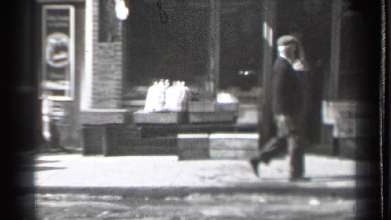 A bundled adult walks along a sidewalk past boxes and brick storefronts.