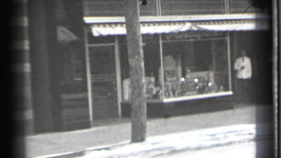 1939 Danielson storefront frame with a person near a display window, striped awning, brick facade, and utility pole.