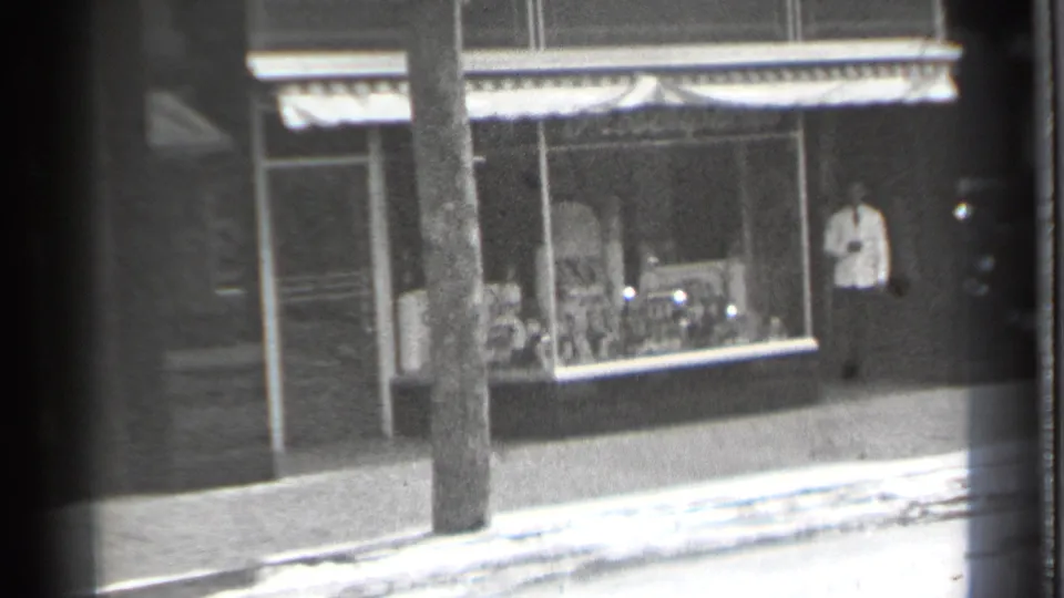 1939 Danielson, Connecticut storefront seen from a moving 8mm camera, with a man standing near the doorway and a utility pole in front.