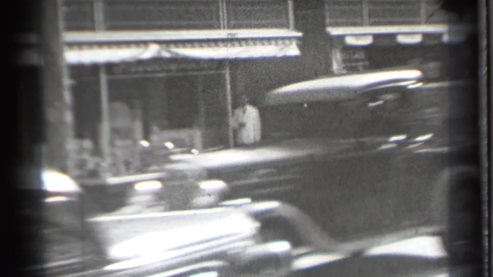 A period automobile blurs across the foreground of the 1939 Danielson street scene, partly obscuring the storefront and doorway figure.