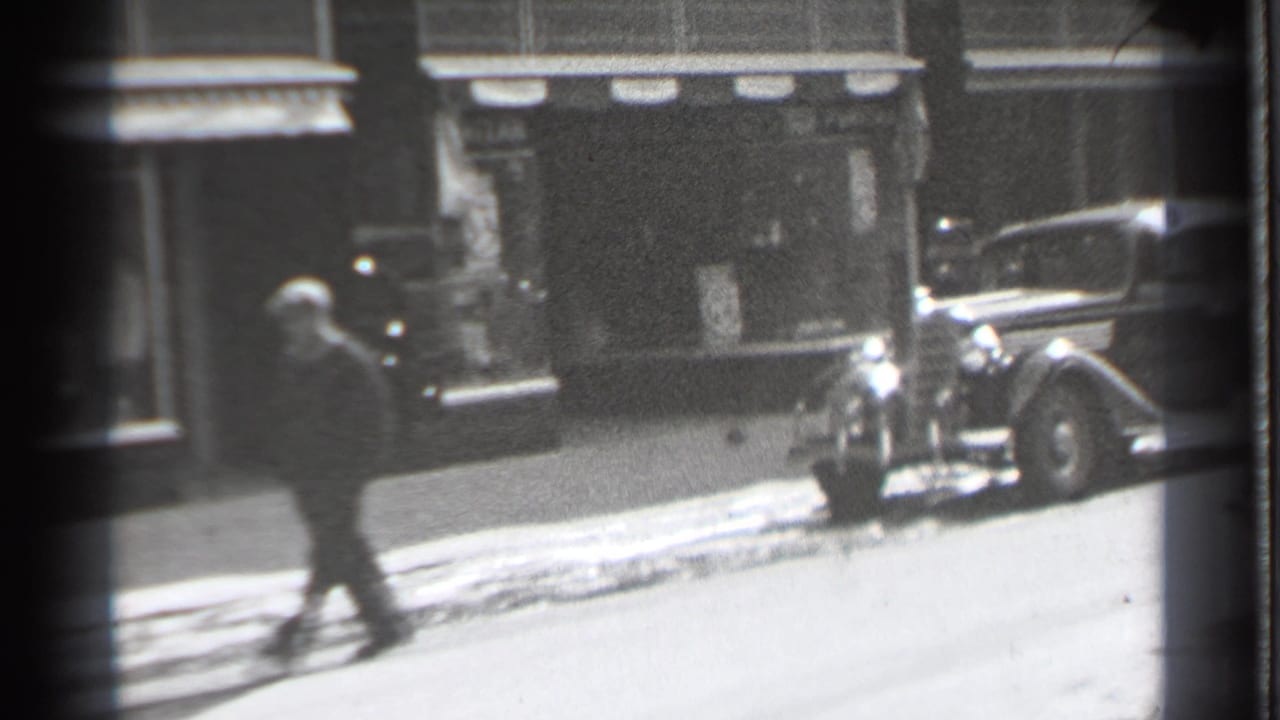 Pedestrian walking past a parked old sedan on a snowy street.